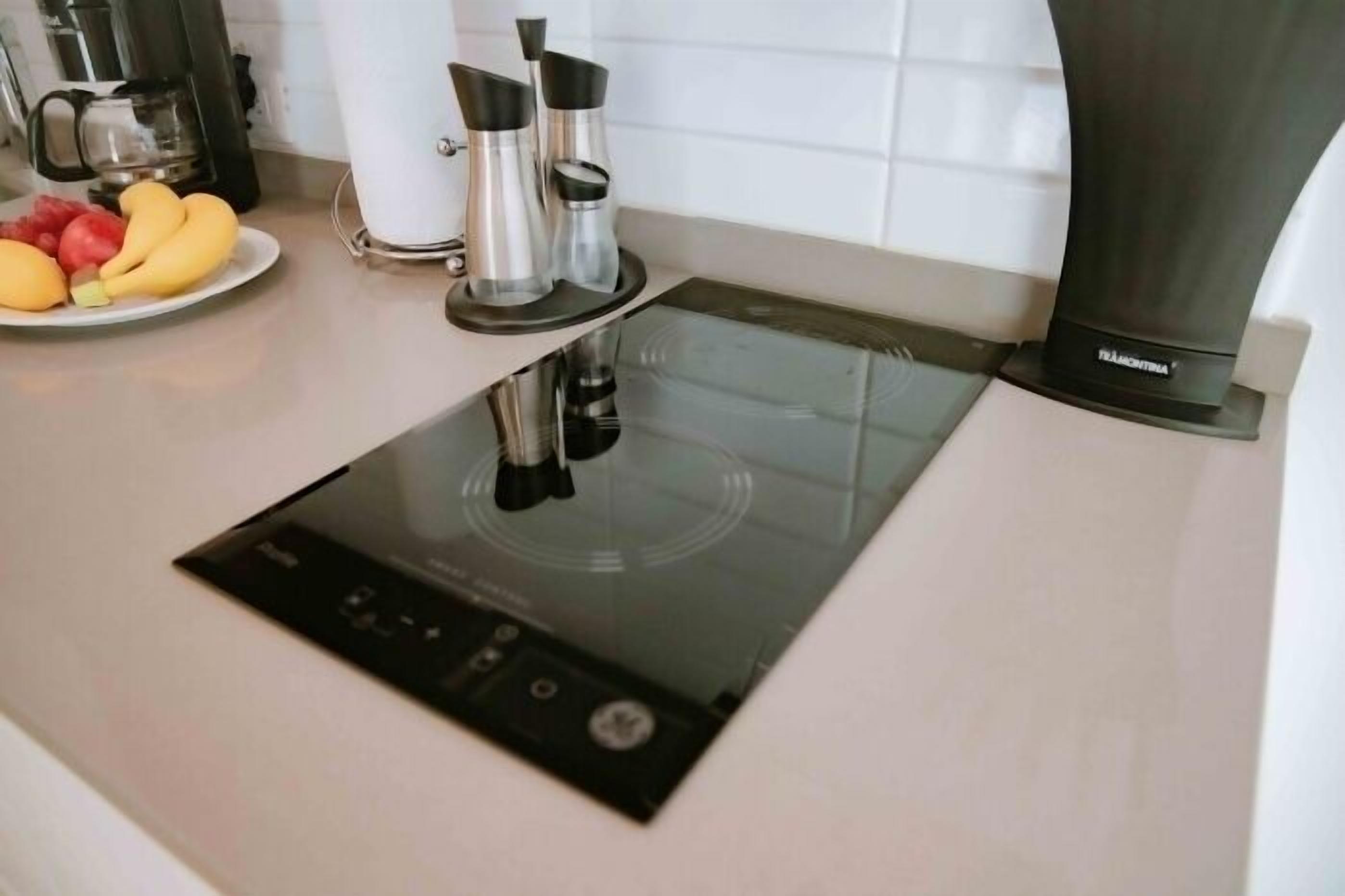 Een moderne keuken met een geïntegreerde inductiekookplaat, een koffiezetapparaat en een schaal fruit.