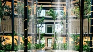 En flerniveauet atriumgård med et centralt vandelement, omgivet af grønt og moderne arkitektur.
