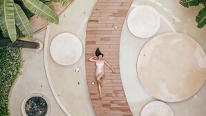 A person lying on a brick pathway surrounded by circular planters and large white circles, with greenery on the sides. - PH8C PANOR, Luxury Penthouse Alberca Privada-2 (Tulum)