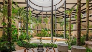 A circular atrium with a glass ceiling, surrounded by lush greenery and modern seating. - PH7B PANOR, Private Paradise in Tulum-2 (Tulum)