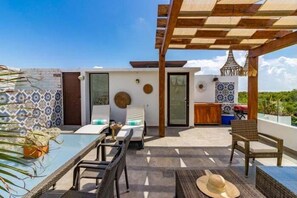 Ein moderner Außenbereich mit einem Glastisch, Korbstühlen und einer Holzpergola.
