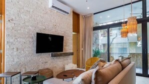 Ein modernes Wohnzimmer mit einer Steinwand, einem Flachbildfernseher, einer Couch, einem Couchtisch und einem Esstisch.