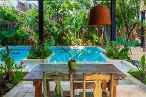 A poolside area with a wooden table and chairs, surrounded by lush greenery and a view of a swimming pool. - VISCOUNT III, New and Big Apartment-2 (Tulum)