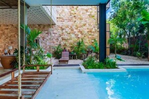 A poolside area with a stone wall, wooden deck, and lush greenery. - VISCOUNT III, New and Big Apartment-2 (Tulum)