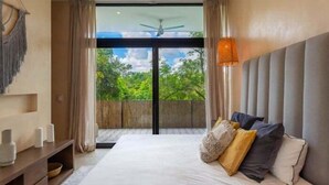 Ein Schlafzimmer mit einem großen Bett, einem Deckenventilator, Blick ins Grüne und einem hölzernen Regal mit Dekoration.