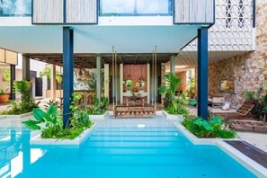 Ett poolområde med en överbyggd sittplats och frodig grönska.