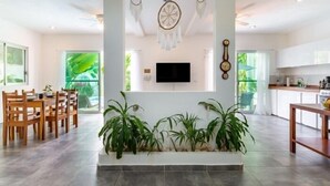 A spacious living area with a flat-screen TV mounted on the wall, a dining area with wooden furniture, and a kitchen with white cabinets. - Casa Alegria, New Villa Private Pool!-2 (Tulum)
