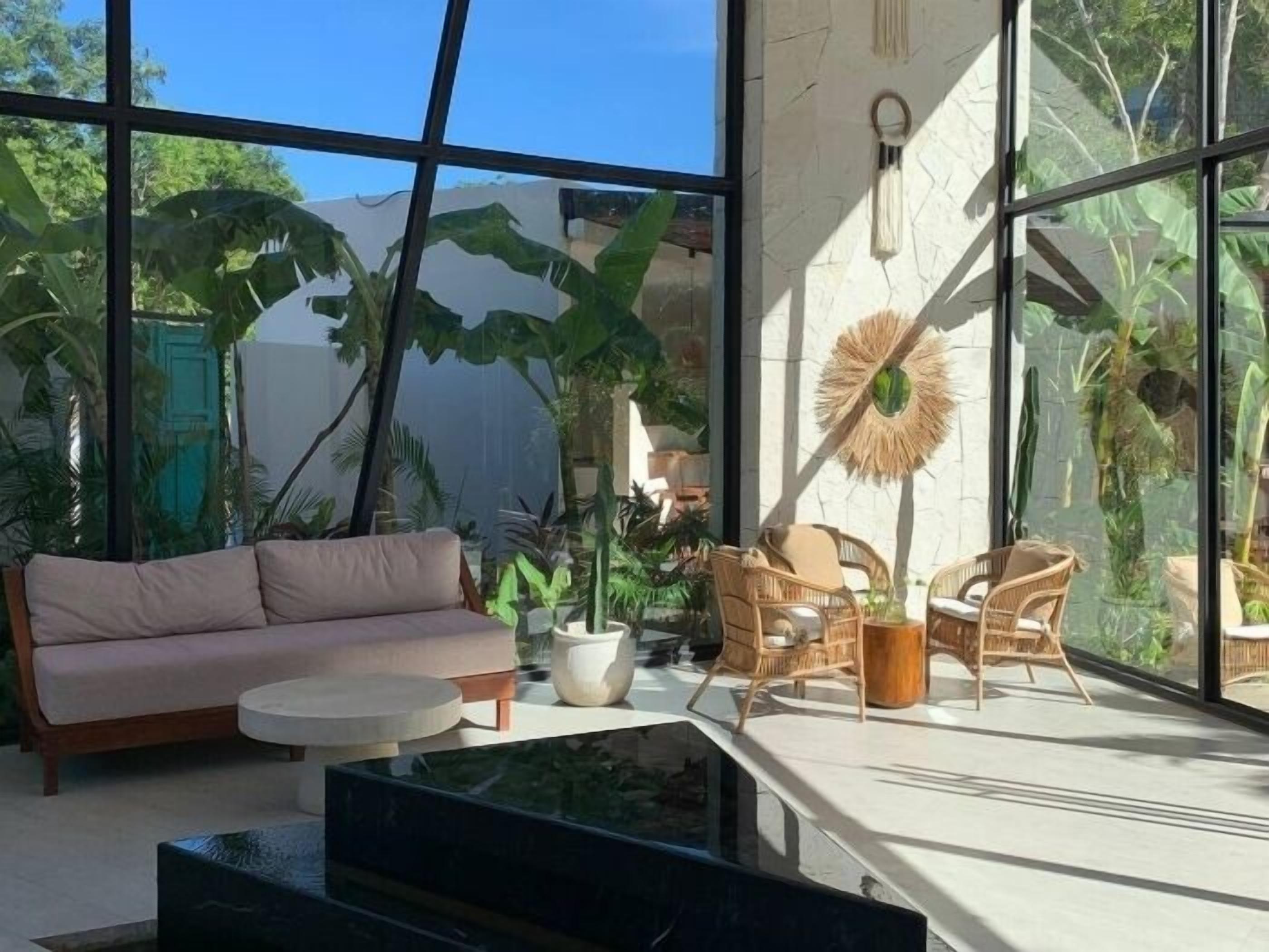 A modern interior with large windows, a sofa, wicker chairs, and a coffee table.