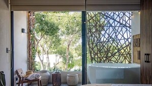 Ein Zimmer mit einer großen Schiebeglasdoor zum Balkon, einer Badewanne und einem Bett, auf dem ein Hut liegt.