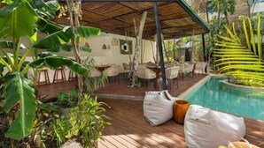 Ein Außenbereich mit Terrasse, Pool und üppiger Bepflanzung sowie Holzmöbeln.