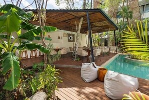 An outdoor patio area with a pool, surrounded by lush greenery and wooden furniture. - Dk jade 30, Luxurious studio with great amenities-2 (Tulum)