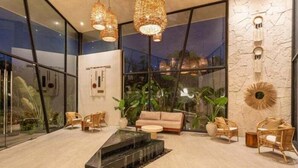 Ein modernes Interieur mit Kamin, Korbmöbeln und großen Fenstern, die einen Blick ins Grüne bieten.