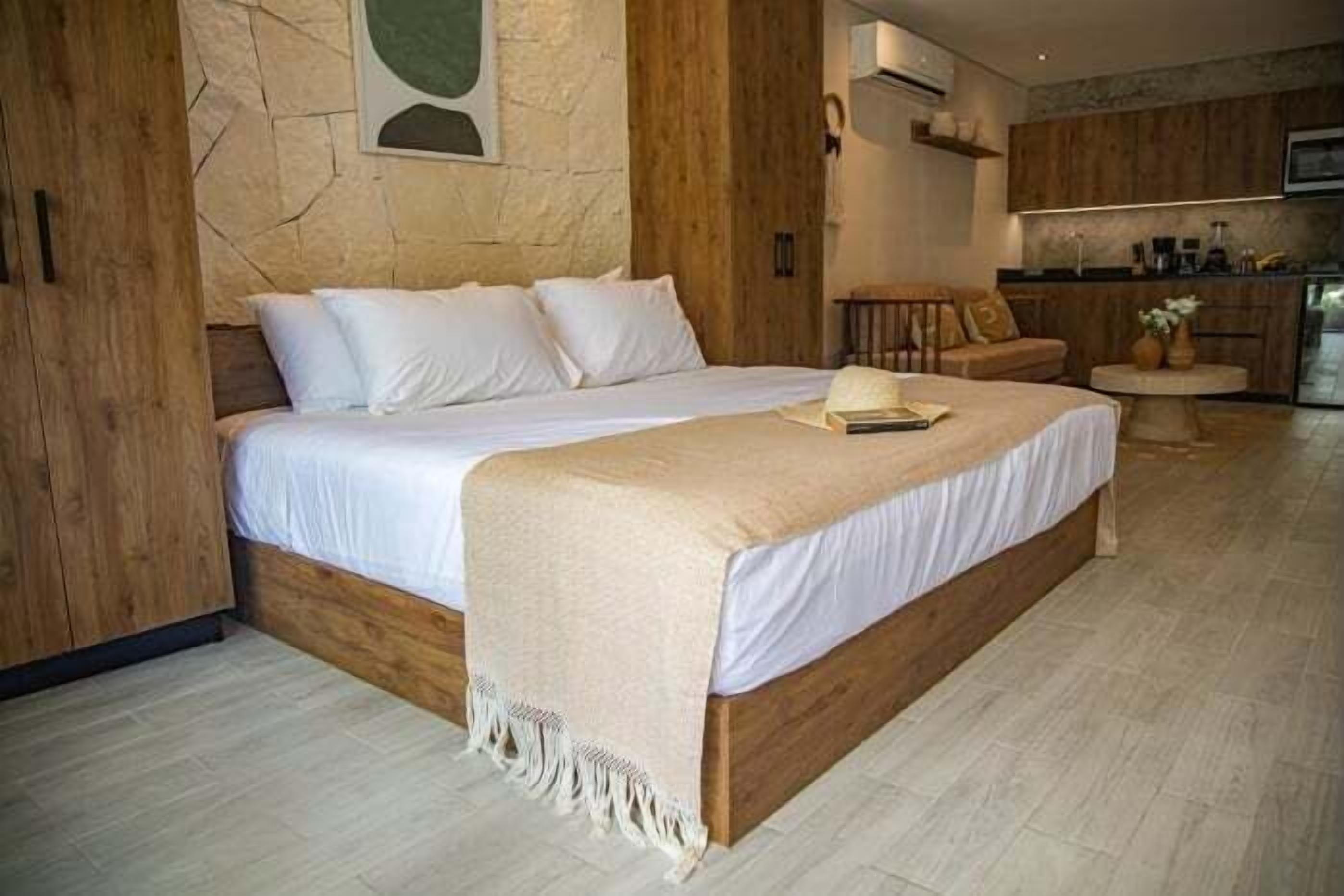 A modern bedroom with a large bed, wooden headboard, and a small seating area with a chair and table.