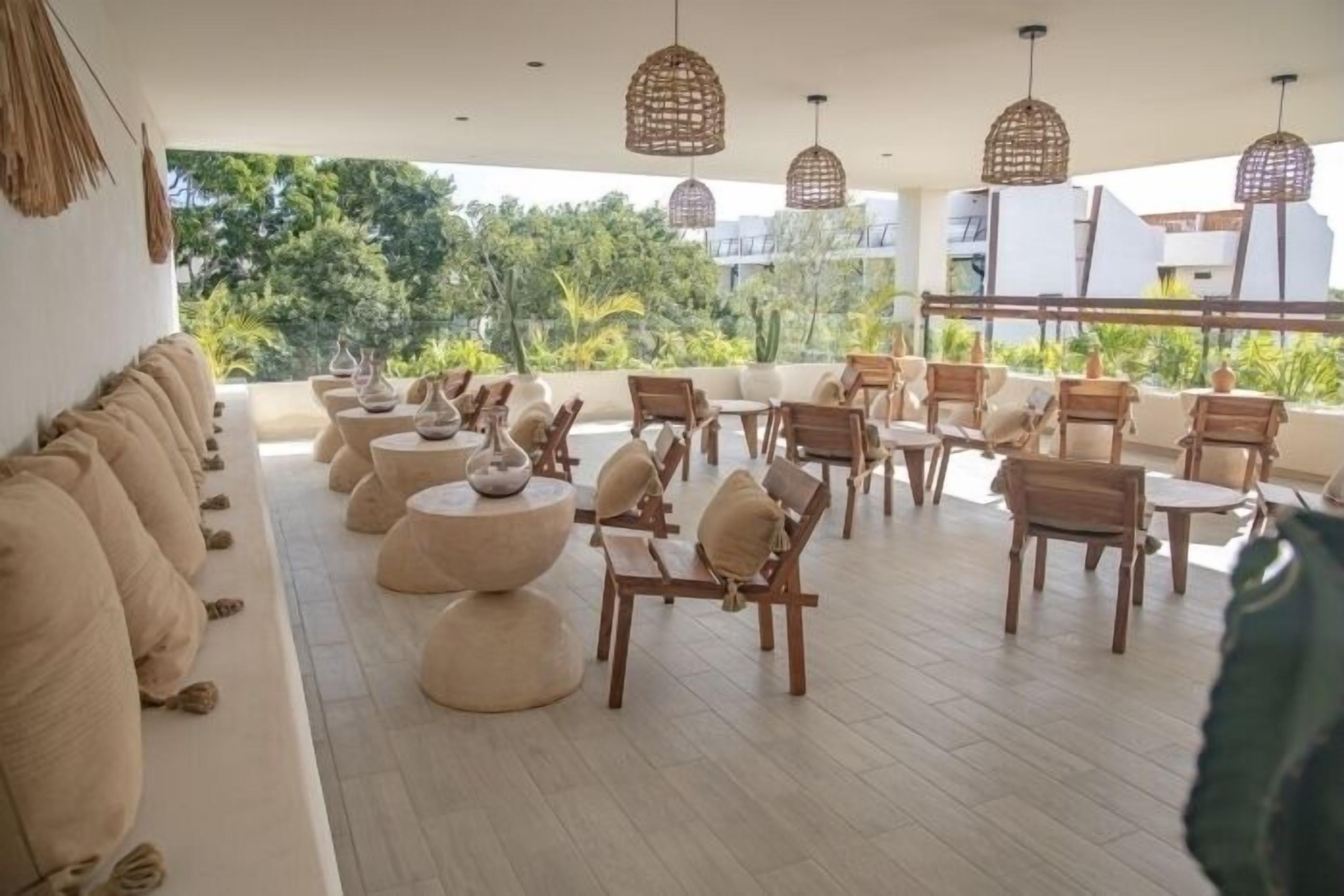 A rooftop lounge area with wooden furniture, round tables, and hanging wicker lamps.