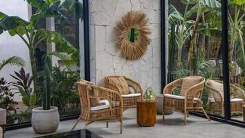 Une pièce meublée de mobilier en osier, agrémentée de grandes plantes en pot et dotée d’un mur à texture.