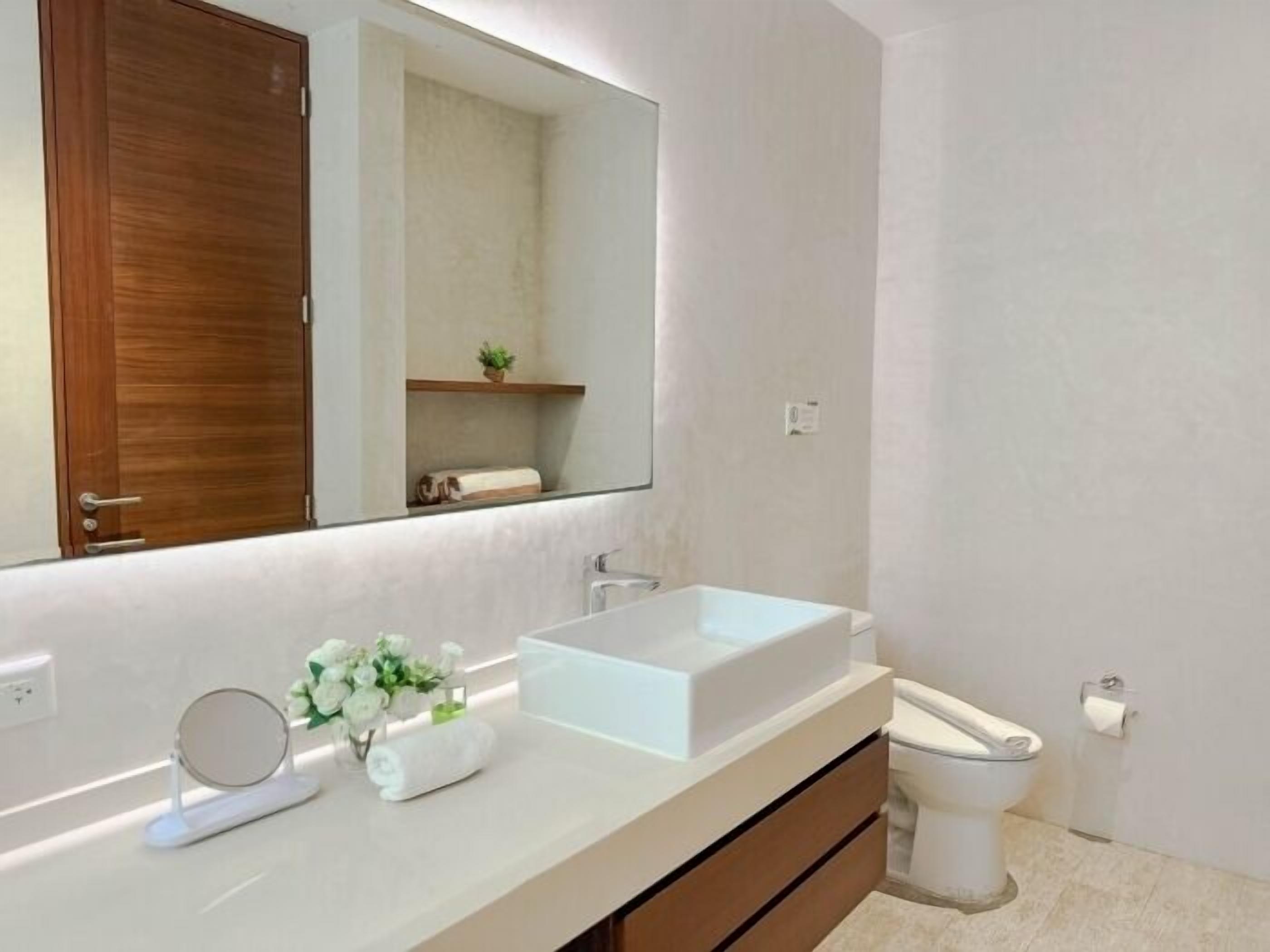 Ein modernes Badezimmer mit einem großen Spiegel, zwei Waschbecken, einer Toilette und einem Holzschrank.