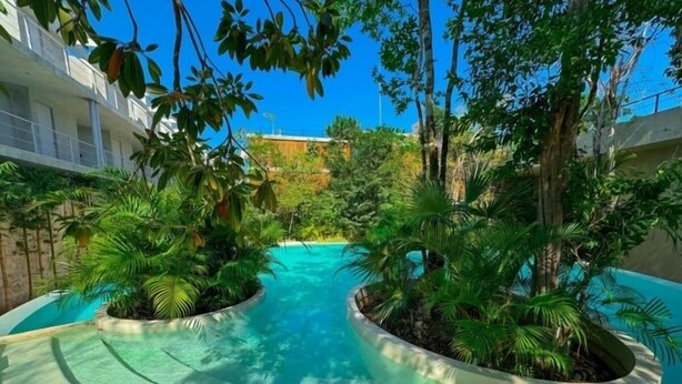 A pool area with two curved water features surrounded by lush tropical plants. - SEREMONIA 206, Tu Refugio Ideal-2 (Tulum)