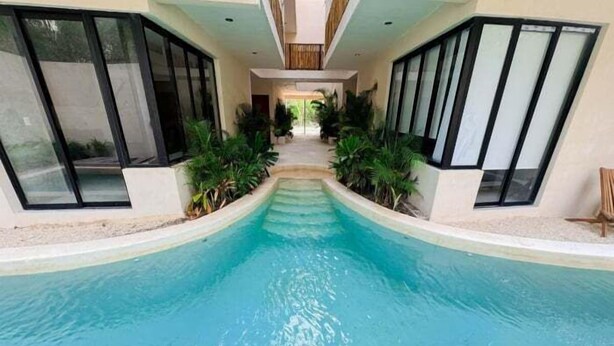 A swimming pool with a curved design, surrounded by large windows and potted plants. - Agata 4, Design and Comfort in Every Corner-2 (Tulum)