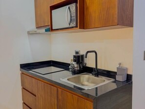 A compact kitchen with a black countertop, a stainless steel sink, a coffee maker, and wooden cabinets. - NAIA C19, Increible Studio Con Jacuzzi (Tulum)