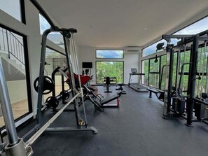 A spacious gym with various exercise equipment, large windows, and a view of greenery outside. - NAIA C19, Increible Studio Con Jacuzzi (Tulum)