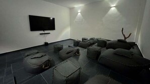 A modern, minimalist room with a flat-screen TV mounted on the wall, a row of grey cushioned seating, and a small tree decoration. - NAIA C19, Increible Studio Con Jacuzzi (Tulum)