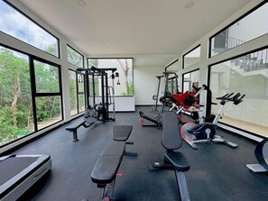 Une salle de sport équipée de divers appareils d’exercice, dotée de grandes fenêtres et offrant une vue sur la verdure.