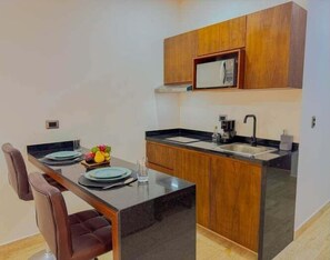 Une cuisine compacte avec des meubles en bois, un plan de travail noir et un coin repas équipé de deux chaises.
