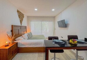 Une chambre d’hôtel comprenant un lit, un bureau avec une chaise, un téléviseur fixé au mur et une fenêtre avec des rideaux.