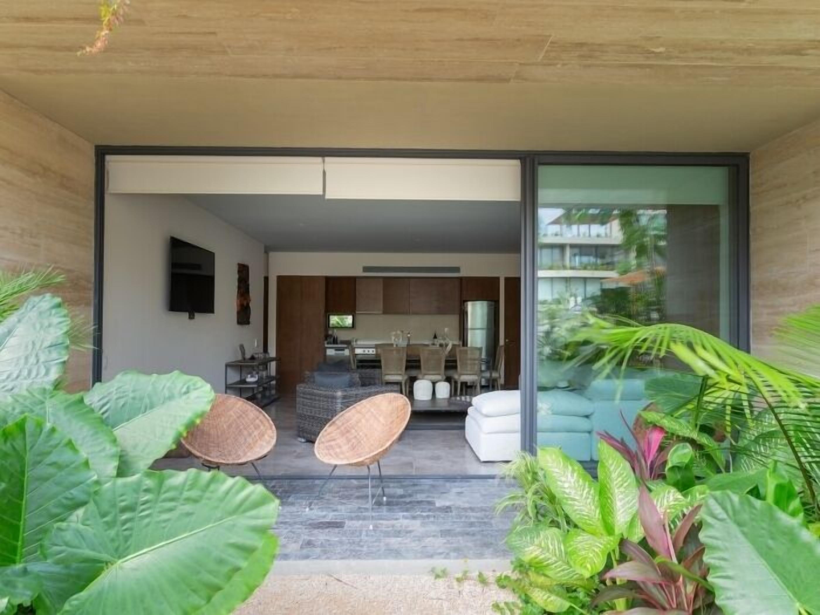 Un interno moderno con zona pranzo, cucina e una porta vetrata che dà su un balcone con piante tropicali.
