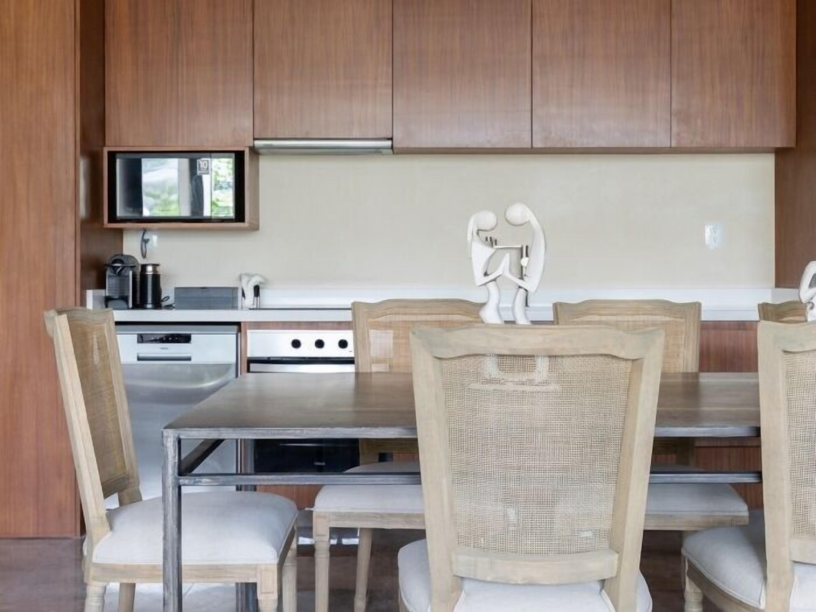 A modern kitchen with wooden cabinets, a stainless steel countertop, and a dining area with wicker chairs and a glass table.