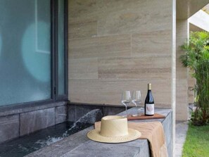 A stone-tiled outdoor area with a wooden table holding a bottle of wine, two glasses, and a straw hat. - MISTIQ TULUM D104, Luxury Two Bedroom (Tulum)