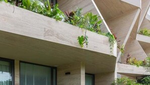 Um edifício moderno com fachada geométrica, varandas com vegetação e grandes janelas.