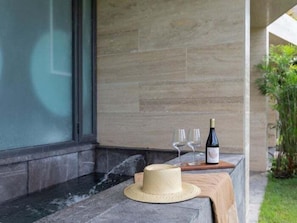 A stone-tiled outdoor area with a wooden table holding a bottle of wine, two glasses, and a straw hat. - MISTIQ TULUM D104, Luxury Two Bedroom-2 (Tulum)