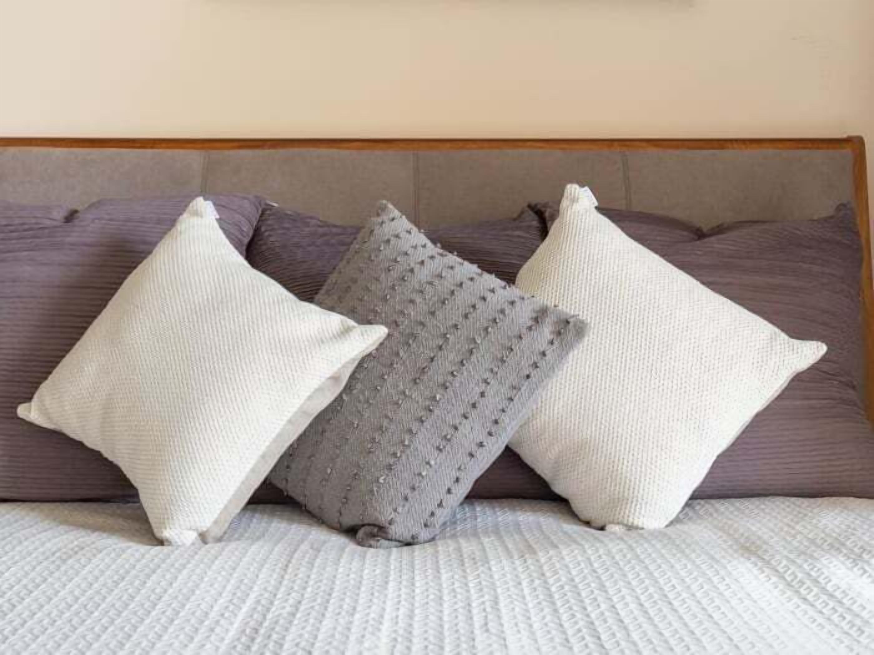 A bed with a headboard, three pillows, and a textured blanket.