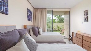 Ein Schlafzimmer mit zwei Betten, einer hölzernen Kommode und einer Schiebetür zum Balkon.