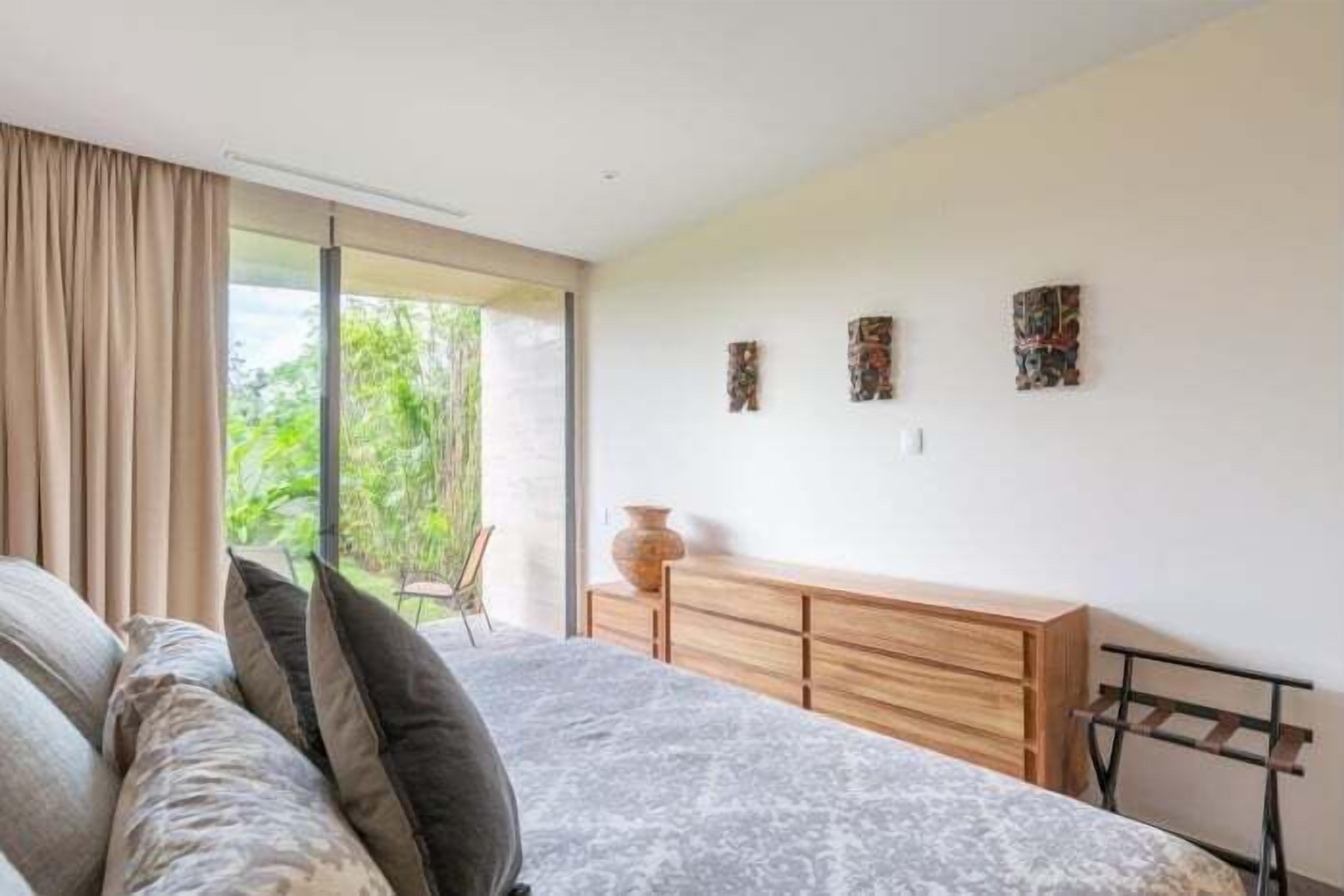 A bedroom with a bed, a wooden dresser, and a window with curtains.