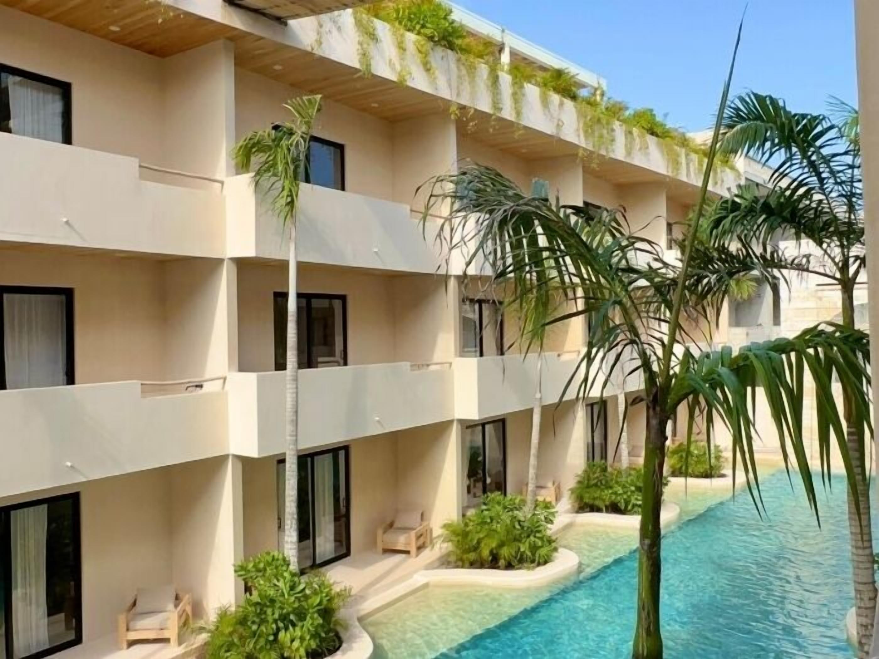 Un hotel a più piani con balconi, piscina e verde lussureggiante.