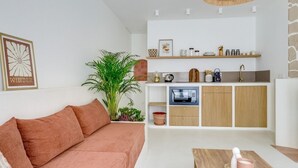 A compact living space with a sofa, a dining table, a kitchen area with a microwave, and a hanging light fixture.