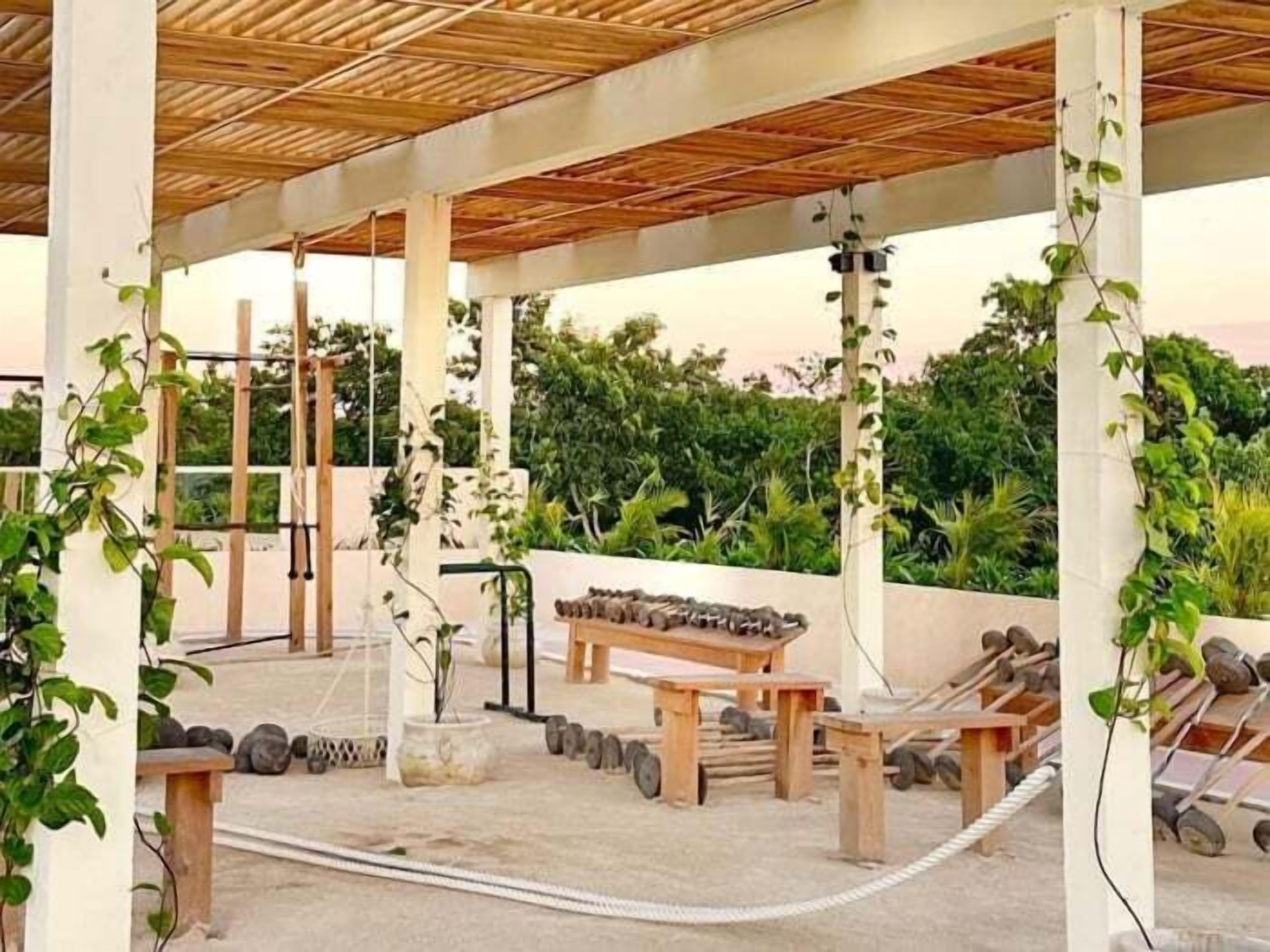 An outdoor covered area with wooden beams, stone benches, and a rope barrier.