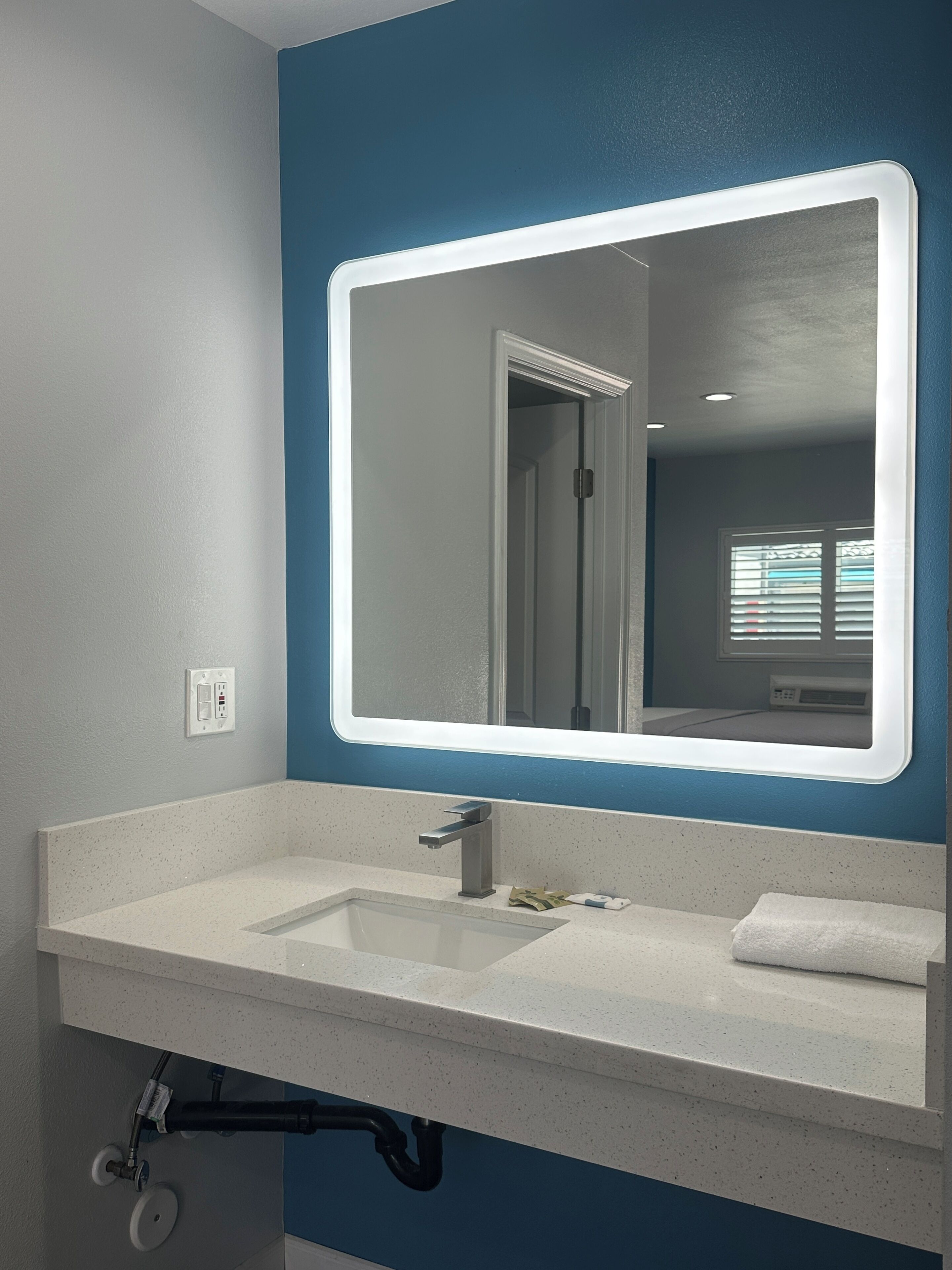 Une salle de bain avec un lavabo blanc, un miroir doté d’un cadre lumineux et un mur bleu.