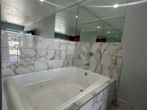 Ein modernes Badezimmer mit Marmorfliesen, einer Glaskabine für die Badewanne und einem großen Spiegel.