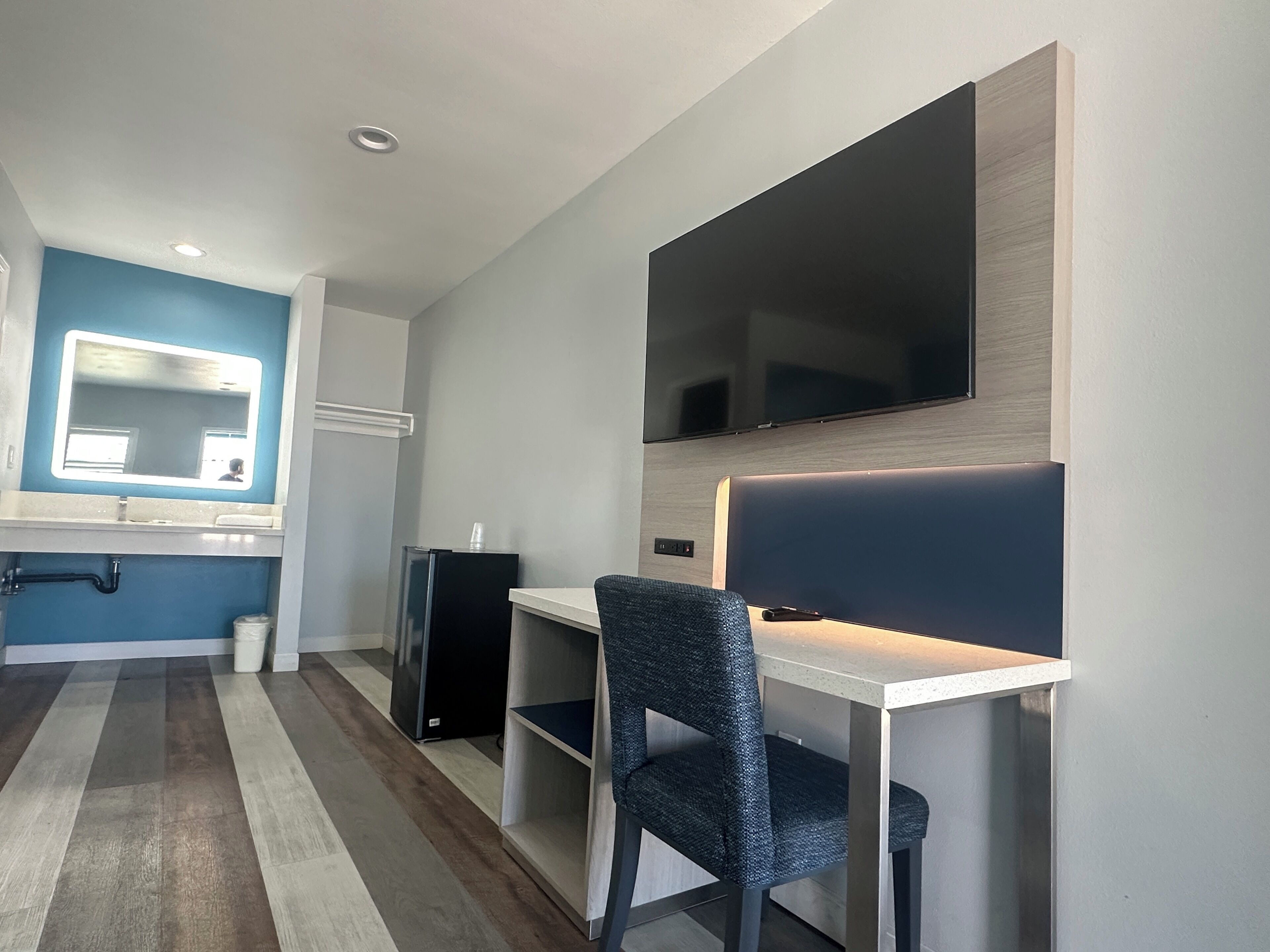 A modern bathroom with a blue accent wall, a mirror, a toilet, and a sink.
