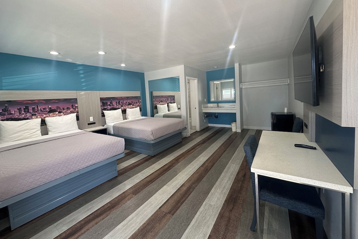 A hotel room with two beds, a desk, a TV, and a cityscape view.