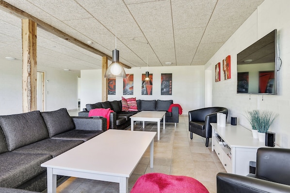 A modern living room with a sectional sofa, a white coffee table, a black leather armchair, and a dining area with a white table and chairs.