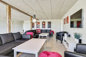 Una sala de estar moderna con un sofá seccional, una mesa de centro blanca, un sillón de cuero negro y un comedor con mesa y sillas blancas.