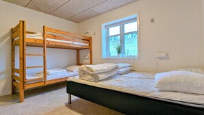 Huoneessa on kerrossängyt, ikkunassa on kukka ja siinä on myös yöpöytä.