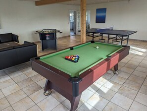 A pool table with balls, a foosball table, and a ping pong table in a room with tiled flooring and a wooden ceiling. - Hanklit holiday home, event & course venue (Nykøbing M)
