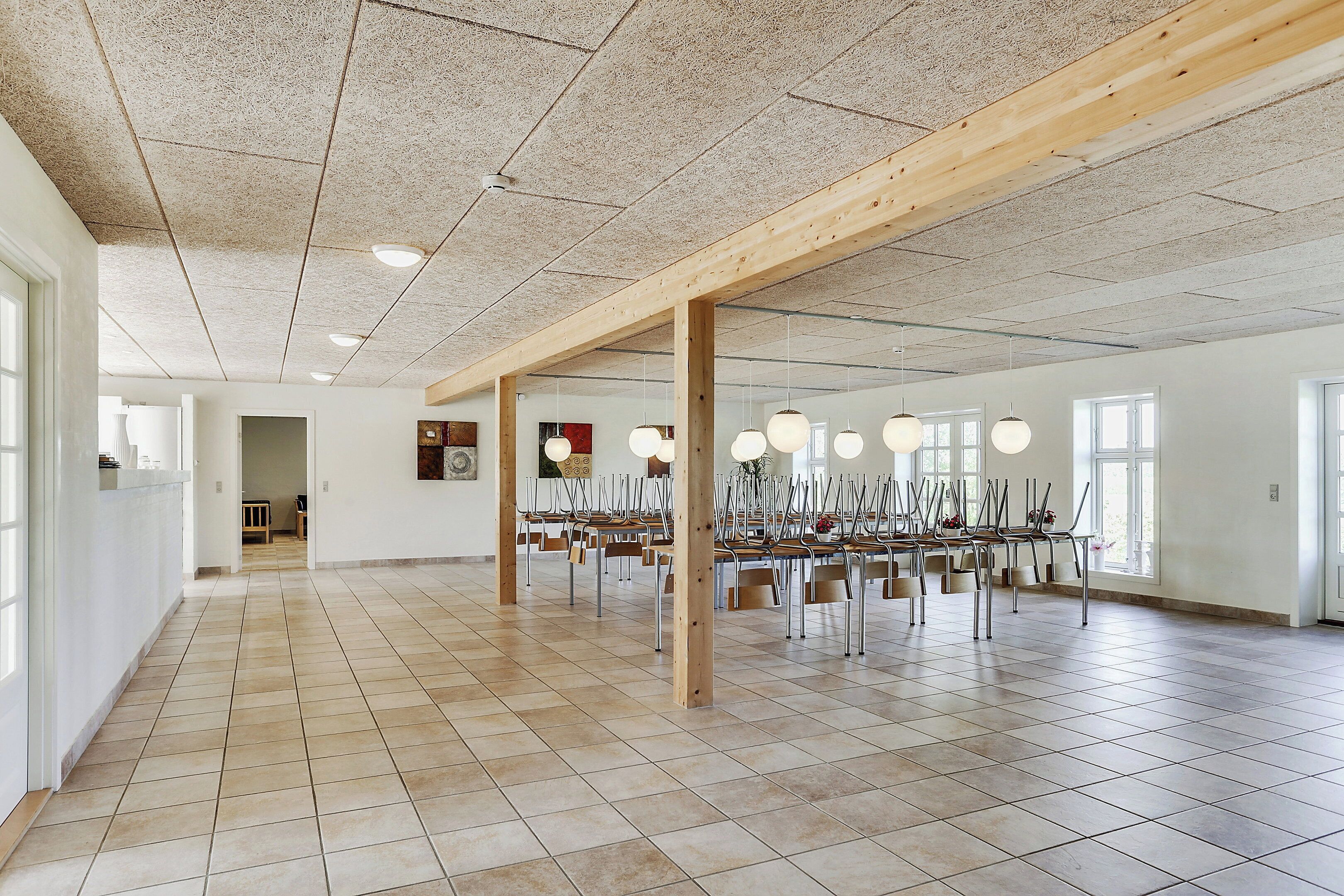 Una habitación amplia con suelo de baldosas, vigas de madera y varias mesas con sillas.
