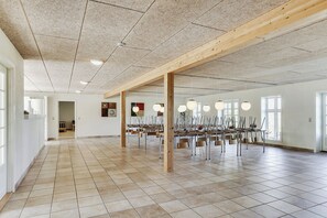 Une pièce spacieuse dotée d’un sol carrelé, de poutres en bois et de plusieurs tables accompagnées de chaises.
