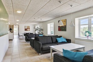 A modern living room with a sofa, a dining area, and a kitchen in the background. - Hanklit holiday home, event & course venue (Nykøbing M)